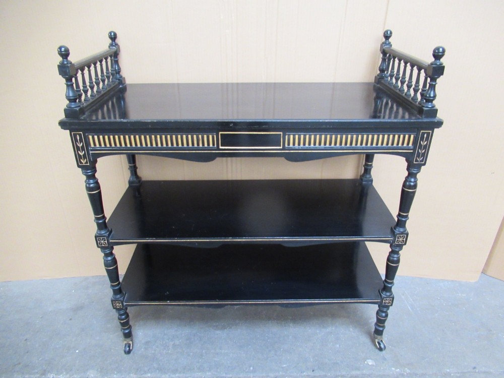 Victorian ebonised three-tier side table featuring spindle side galleries, turned legs, brass castors, and gold fluted detailing on the frieze. View II