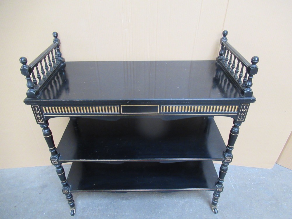 Victorian ebonised three-tier side table featuring spindle side galleries, turned legs, brass castors, and gold fluted detailing on the frieze. View III