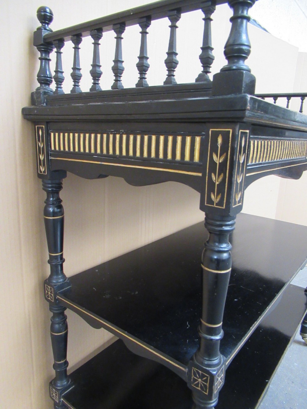 Victorian ebonised three-tier side table featuring spindle side galleries, turned legs, brass castors, and gold fluted detailing on the frieze. View V