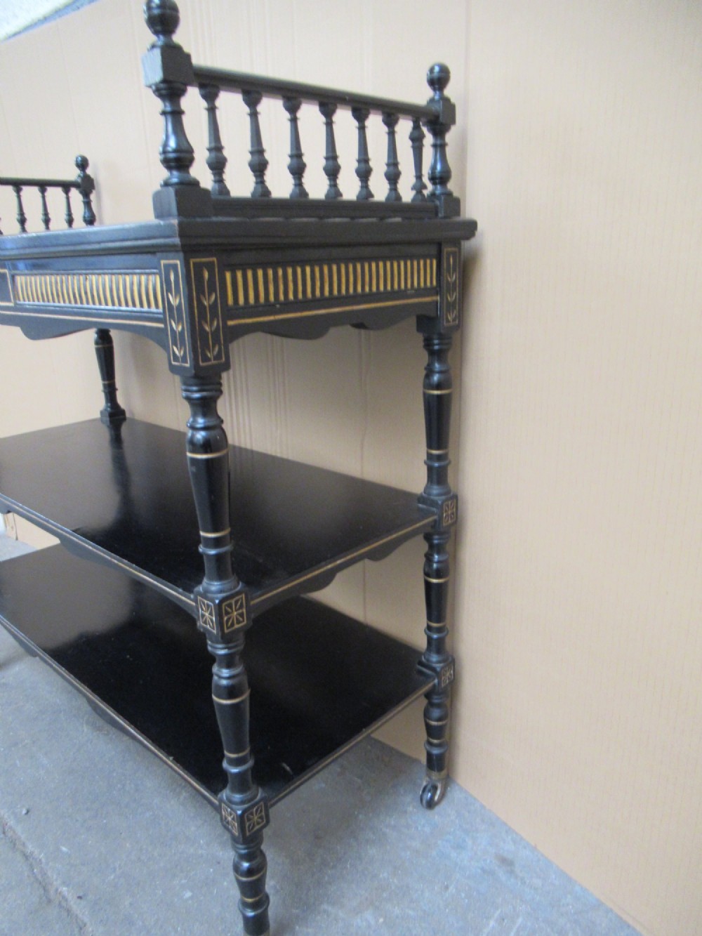 Victorian ebonised three-tier side table featuring spindle side galleries, turned legs, brass castors, and gold fluted detailing on the frieze. View VI