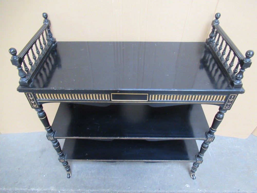 Victorian ebonised three-tier side table featuring spindle side galleries, turned legs, brass castors, and gold fluted detailing on the frieze. View X