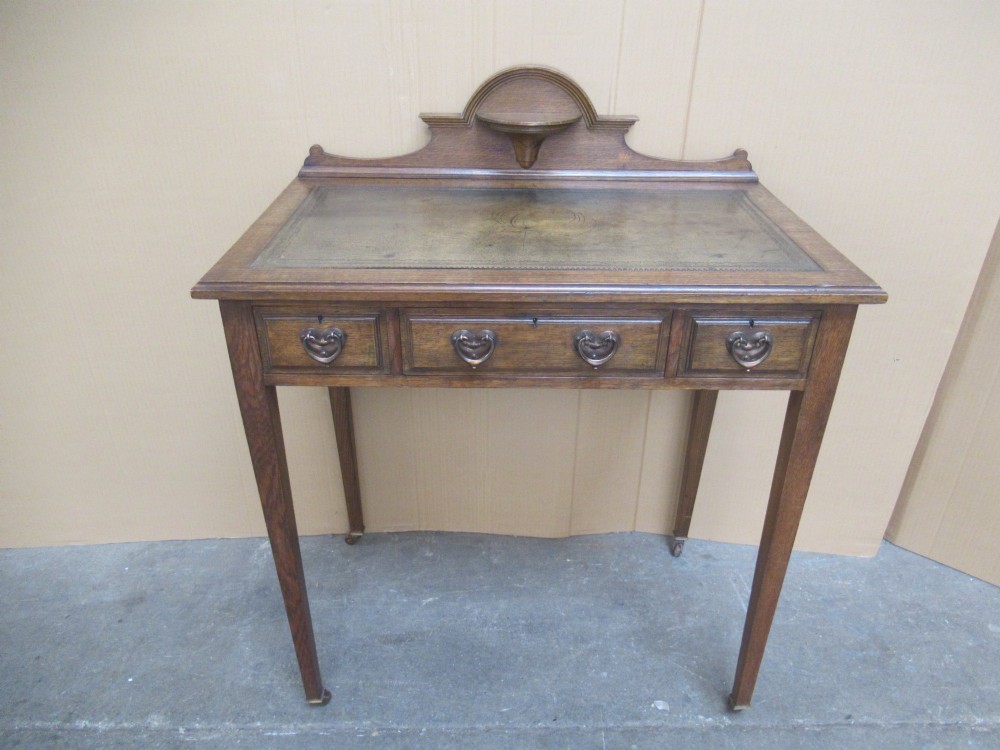 An Edwardian oak writing desk with a leather inset top, three drawers with brass handles, and a raised gallery back featuring a small bracket shelf.