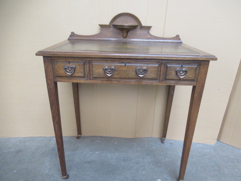 An Edwardian oak writing desk with a leather inset top, three drawers with brass handles, and a raised gallery back featuring a small bracket shelf. View II