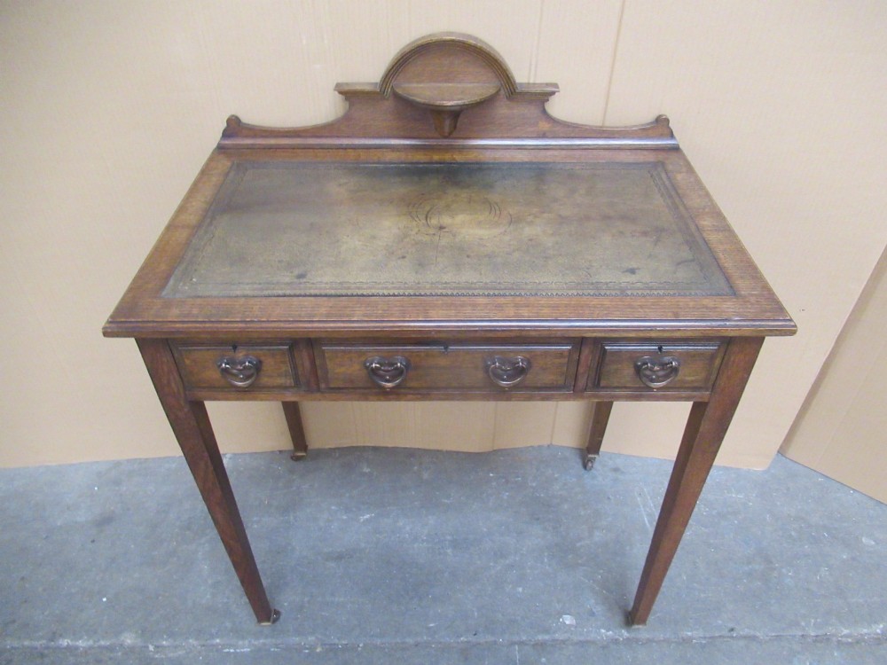 An Edwardian oak writing desk with a leather inset top, three drawers with brass handles, and a raised gallery back featuring a small bracket shelf. View III