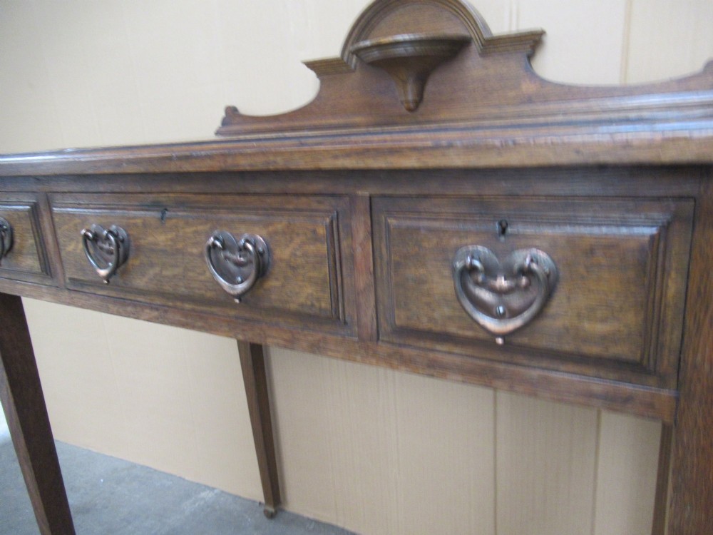 An Edwardian oak writing desk with a leather inset top, three drawers with brass handles, and a raised gallery back featuring a small bracket shelf. View IX