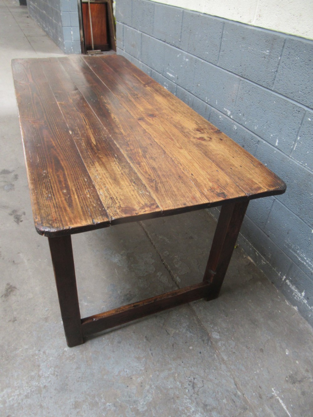 A 19th-century pine dining table with a wide plank top, straight legs, and side stretchers in a warm brown timber finish. View VI