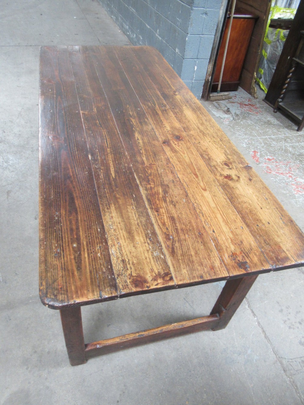 A 19th-century pine dining table with a wide plank top, straight legs, and side stretchers in a warm brown timber finish. View VII