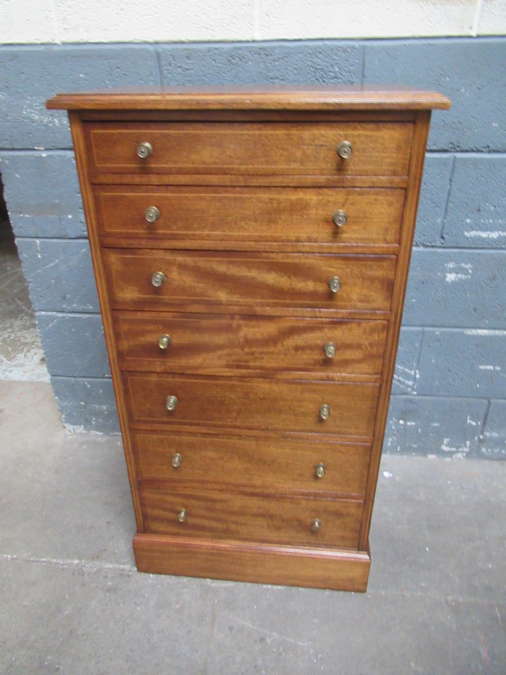An Edwardian mahogany tall and slim chest featuring seven drawers with brass ring handles set on a solid plinth base.
