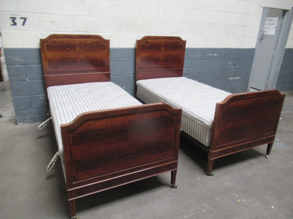 A pair of Edwardian mahogany single beds featuring flame mahogany panels, fine boxwood inlay, and tapered square legs with brass castors. View II