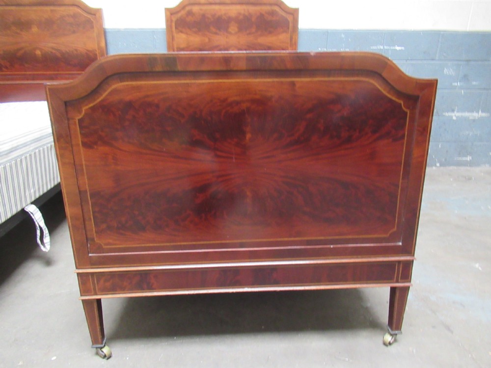 A pair of Edwardian mahogany single beds featuring flame mahogany panels, fine boxwood inlay, and tapered square legs with brass castors. View VI