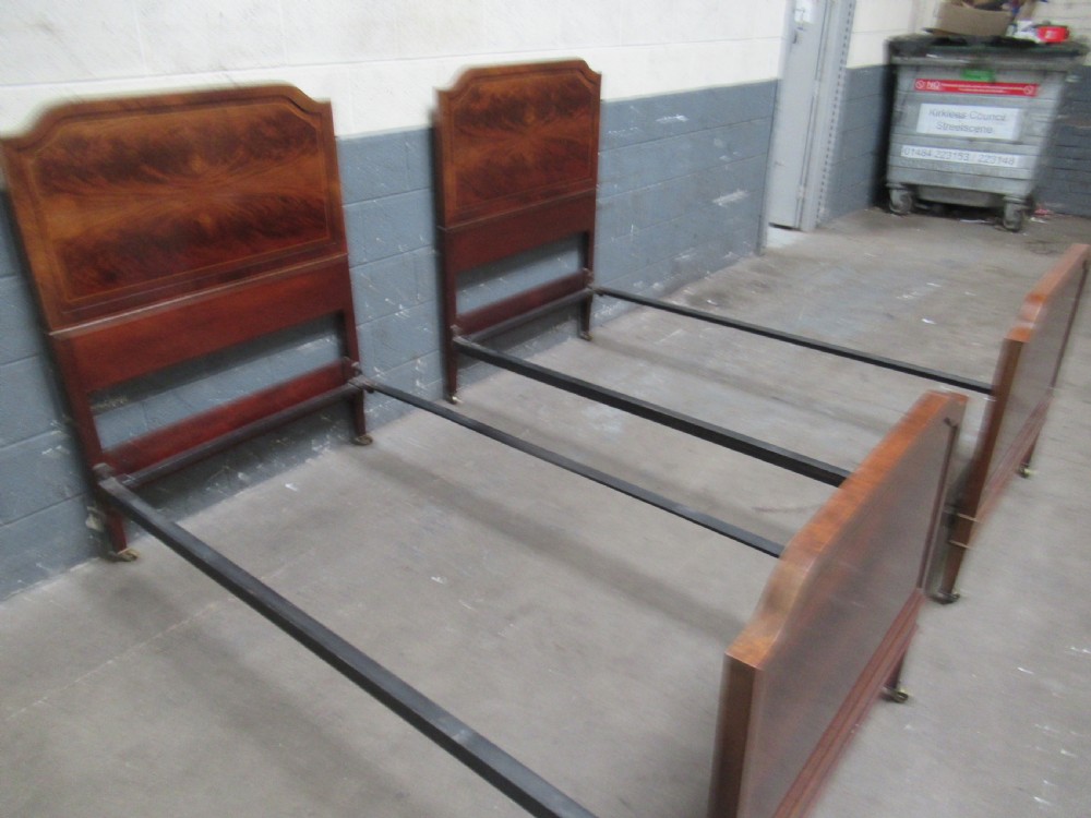 A pair of Edwardian mahogany single beds featuring flame mahogany panels, fine boxwood inlay, and tapered square legs with brass castors. View IX