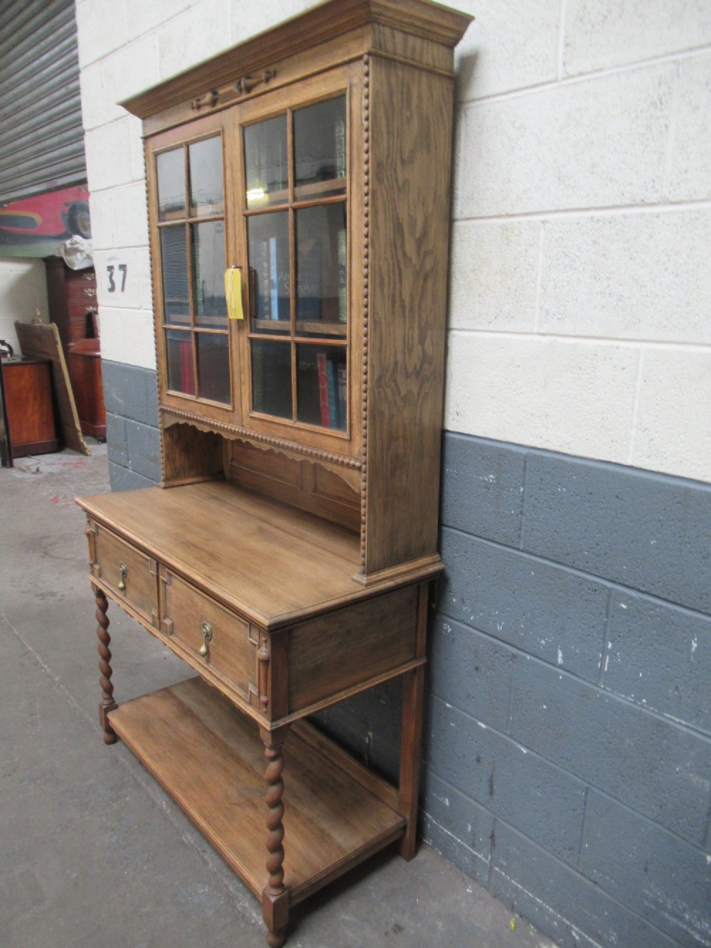 A 1920s oak two-door glazed bookcase featuring upper glass display cabinet, two geometric-moulded drawers, and barley twist legs with a lower undertier shelf. View III
