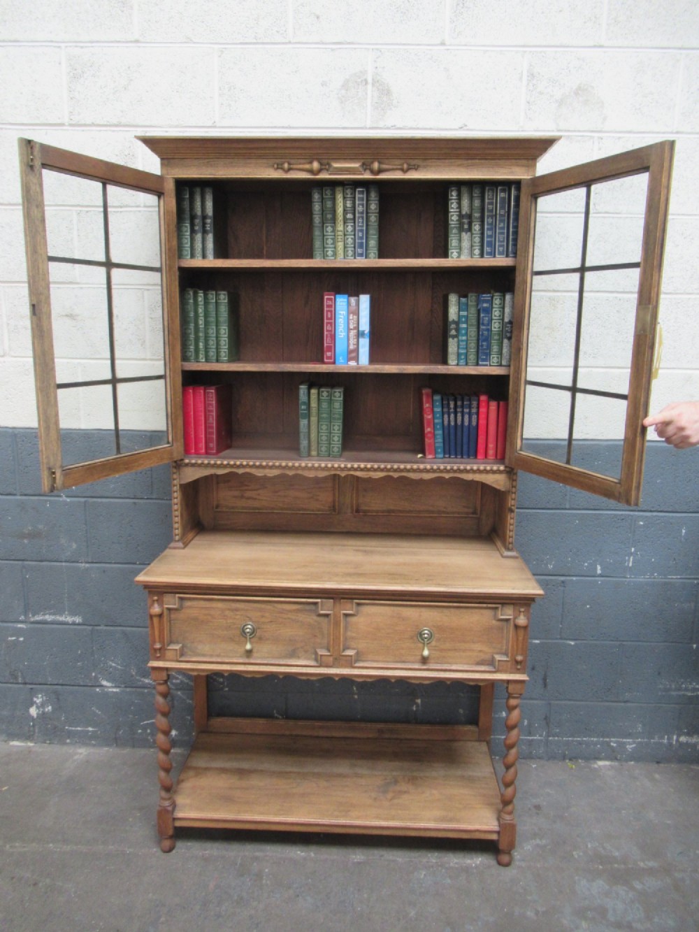 A 1920s oak two-door glazed bookcase featuring upper glass display cabinet, two geometric-moulded drawers, and barley twist legs with a lower undertier shelf. View IV