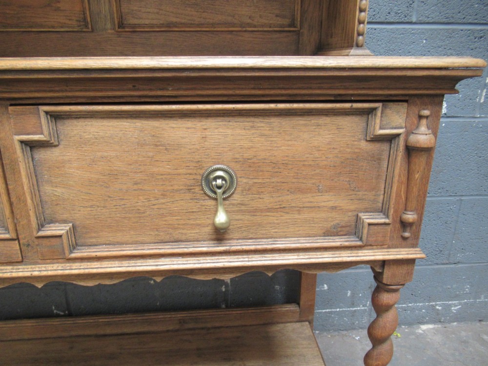 A 1920s oak two-door glazed bookcase featuring upper glass display cabinet, two geometric-moulded drawers, and barley twist legs with a lower undertier shelf. View VIII
