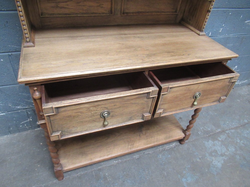 A 1920s oak two-door glazed bookcase featuring upper glass display cabinet, two geometric-moulded drawers, and barley twist legs with a lower undertier shelf. View XI