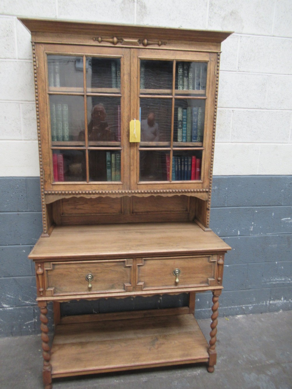 A 1920s oak two-door glazed bookcase featuring upper glass display cabinet, two geometric-moulded drawers, and barley twist legs with a lower undertier shelf. View XII