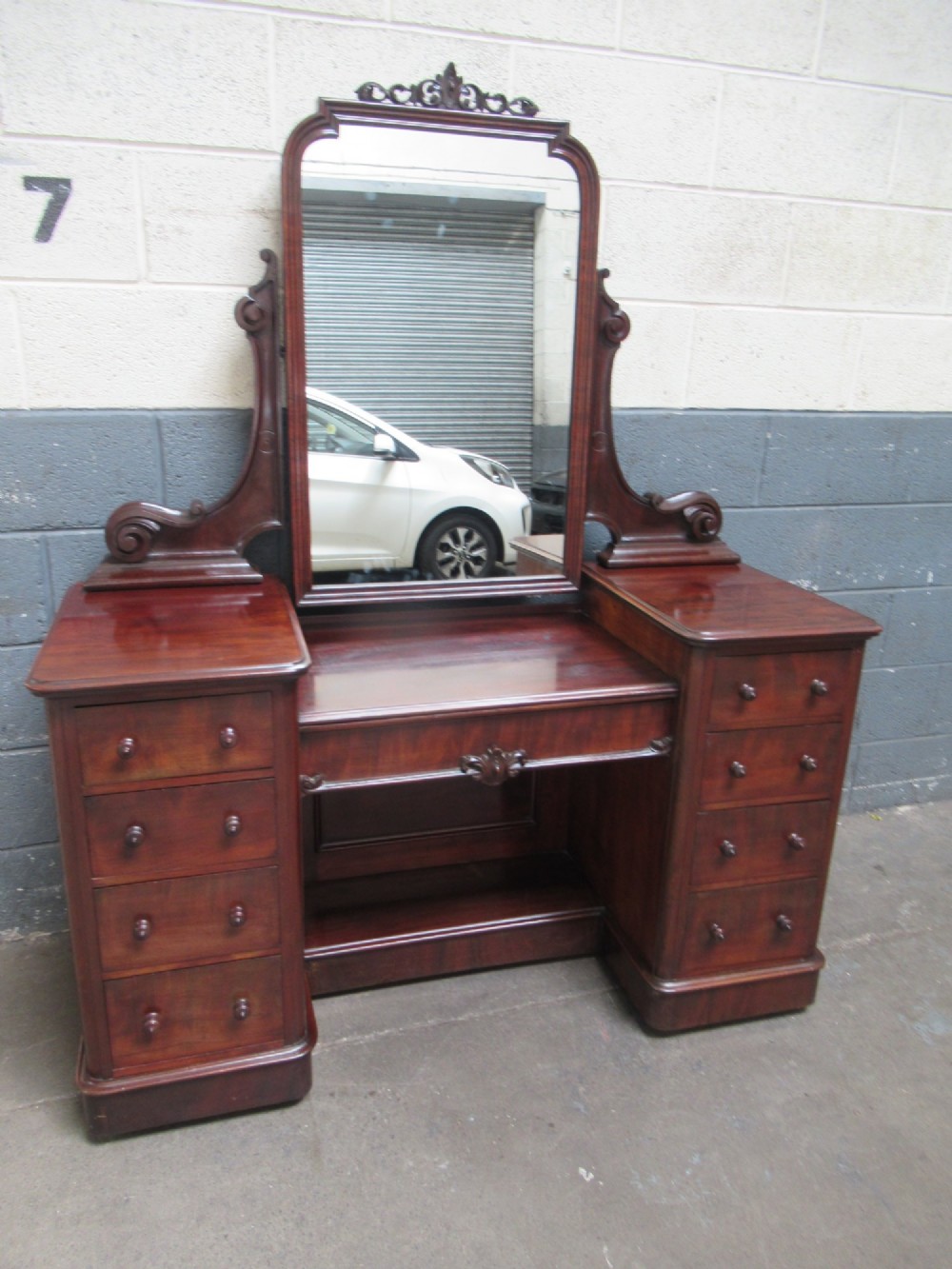 A Victorian mahogany dressing table featuring a central arched swing mirror with carved scroll supports, set above twin pedestals containing drawers with turned wooden handles.