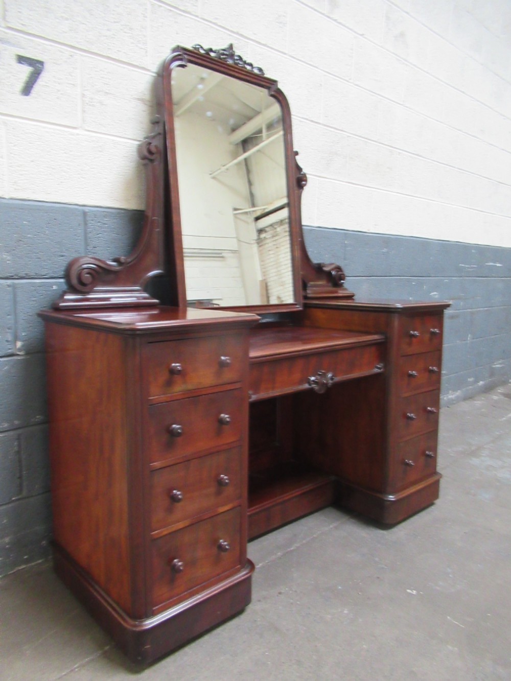 A Victorian mahogany dressing table featuring a central arched swing mirror with carved scroll supports, set above twin pedestals containing drawers with turned wooden handles. View II