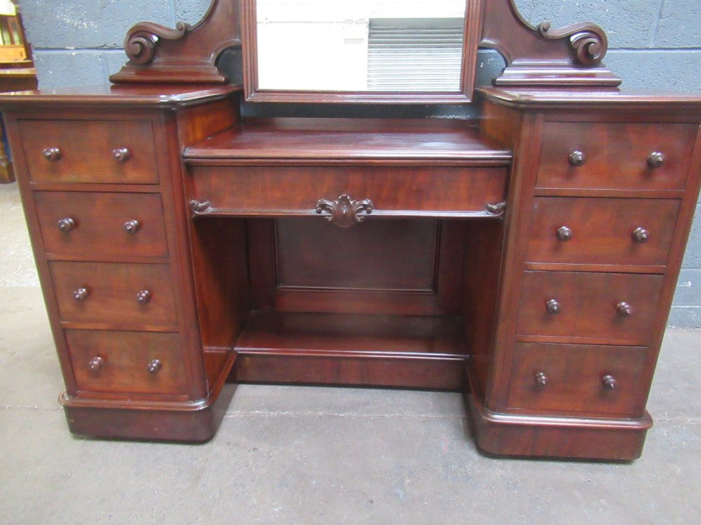 A Victorian mahogany dressing table featuring a central arched swing mirror with carved scroll supports, set above twin pedestals containing drawers with turned wooden handles. View VII