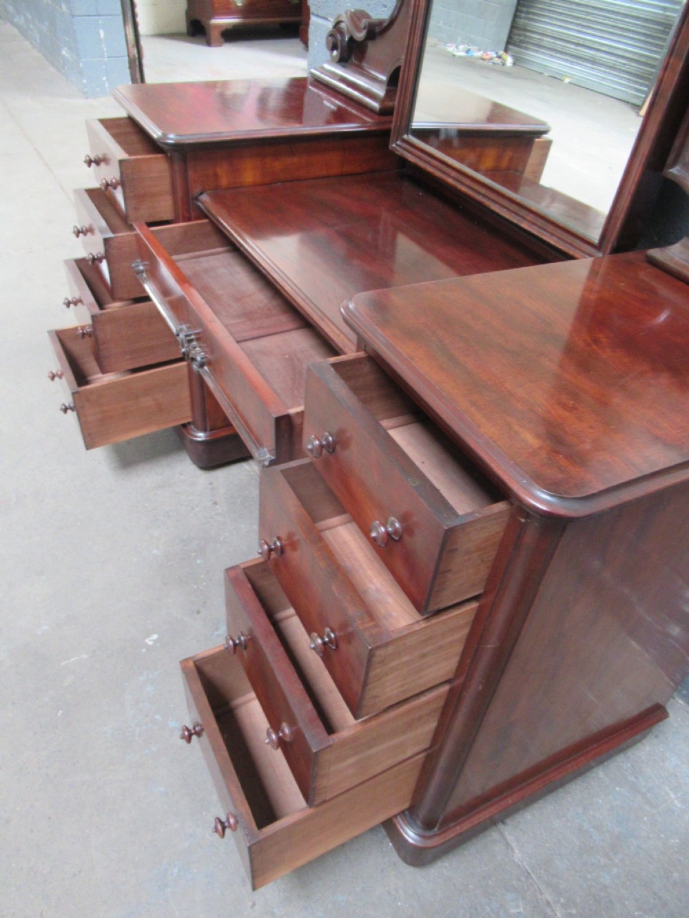 A Victorian mahogany dressing table featuring a central arched swing mirror with carved scroll supports, set above twin pedestals containing drawers with turned wooden handles. View VIII