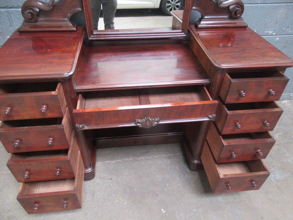 A Victorian mahogany dressing table featuring a central arched swing mirror with carved scroll supports, set above twin pedestals containing drawers with turned wooden handles. View X