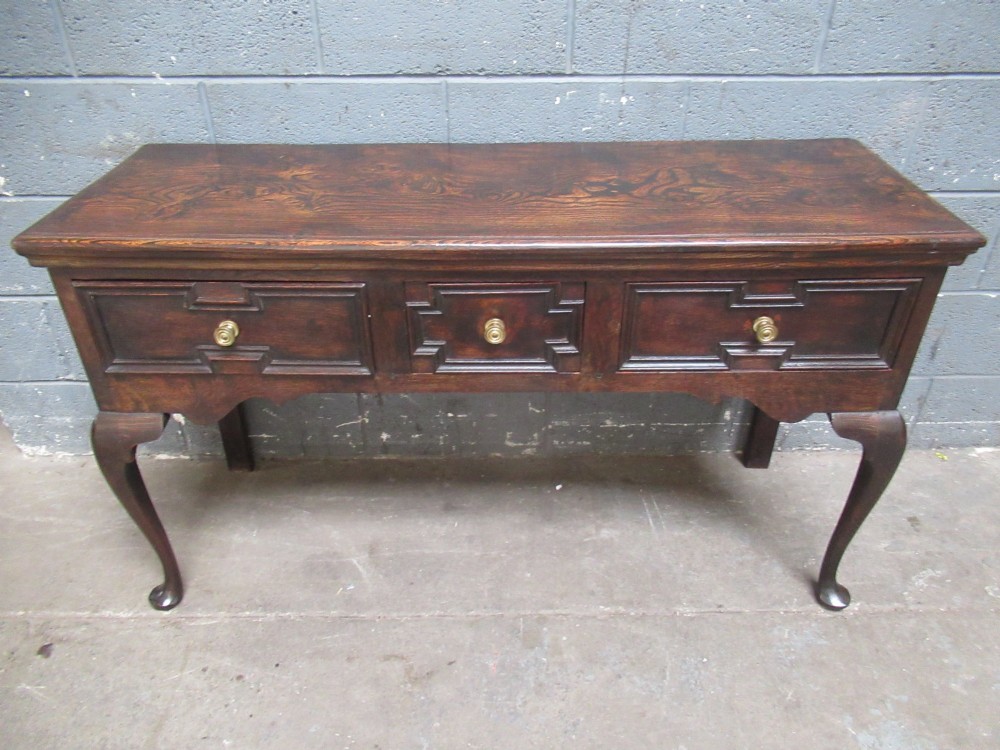 An antique dark oak dresser base featuring three drawers with geometric mouldings and brass knobs, supported by cabriole legs. View II