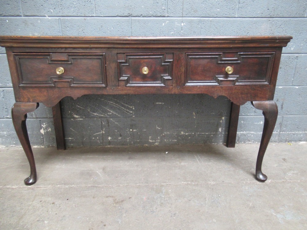 An antique dark oak dresser base featuring three drawers with geometric mouldings and brass knobs, supported by cabriole legs. View III
