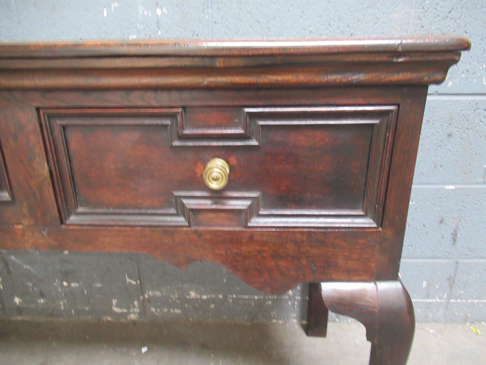 An antique dark oak dresser base featuring three drawers with geometric mouldings and brass knobs, supported by cabriole legs. View IV