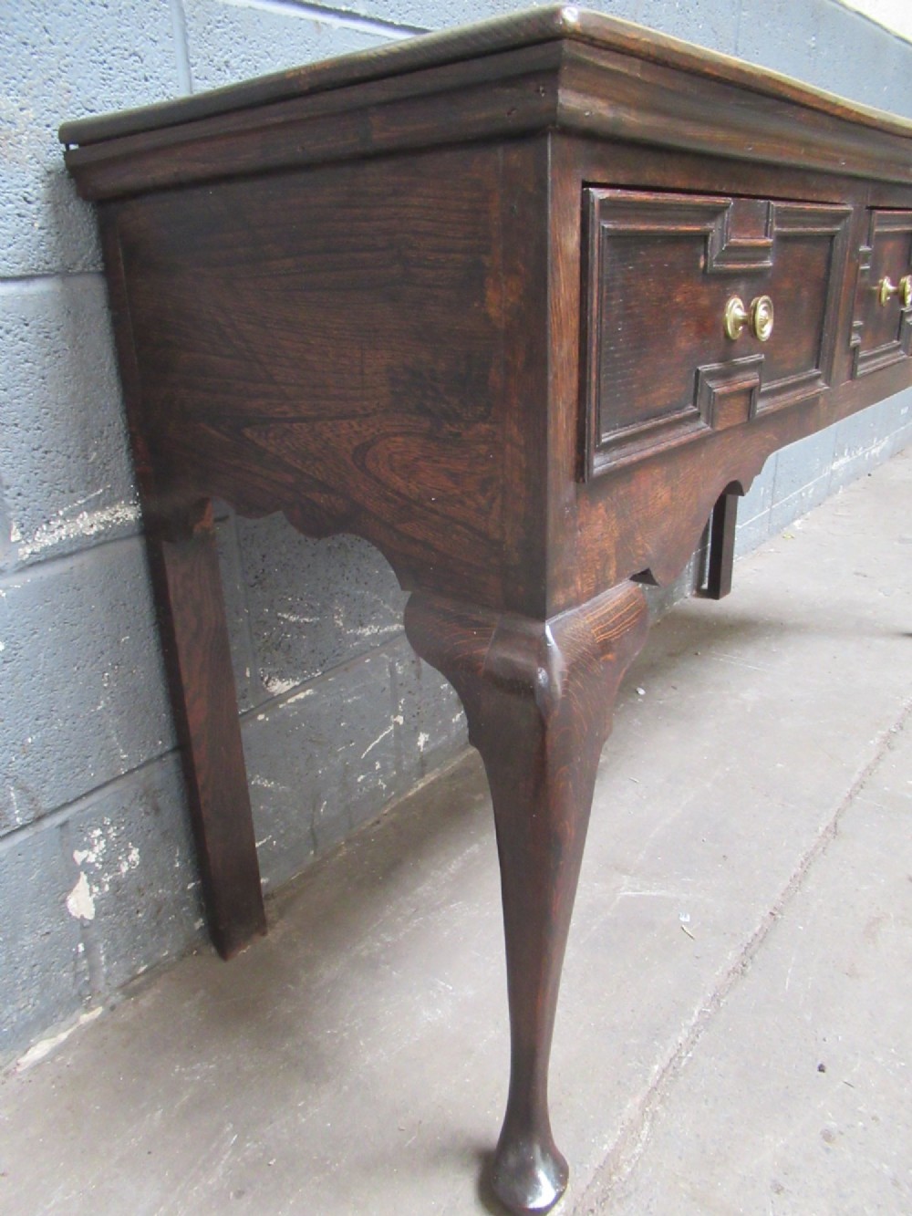 An antique dark oak dresser base featuring three drawers with geometric mouldings and brass knobs, supported by cabriole legs. View VIII