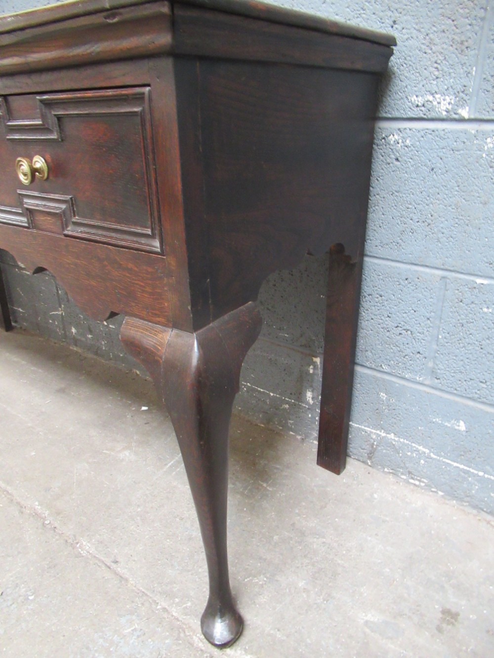An antique dark oak dresser base featuring three drawers with geometric mouldings and brass knobs, supported by cabriole legs. View IX