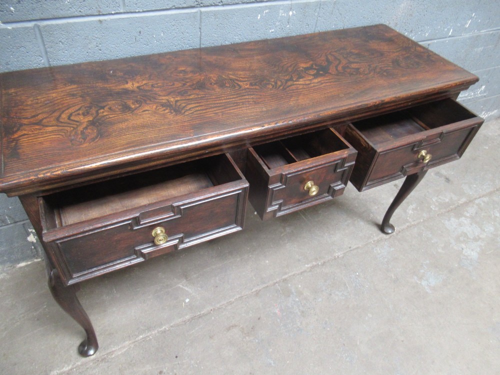 An antique dark oak dresser base featuring three drawers with geometric mouldings and brass knobs, supported by cabriole legs. View XI
