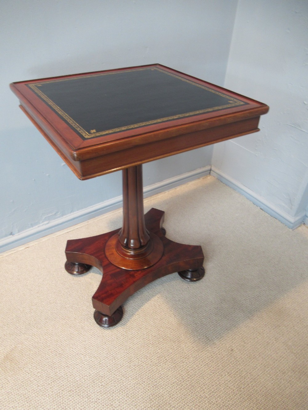 A 19th-century square mahogany side table featuring a dark leather top with gilt tooling, supported by a central turned pedestal and a quadform base. View X