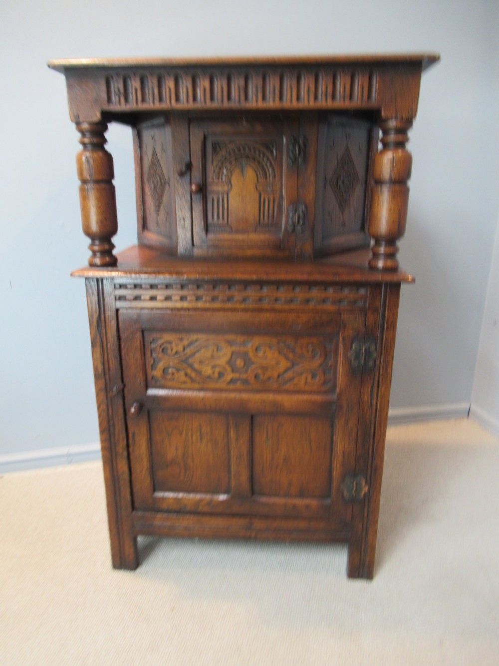 A small carved dark oak court cupboard featuring a two-tiered structure with turned bulbous supports and carved panel doors.