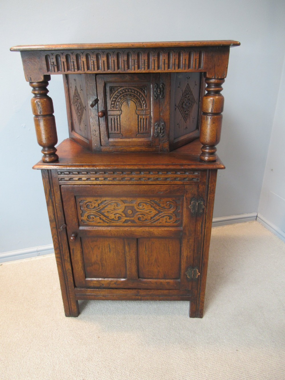 A small carved dark oak court cupboard featuring a two-tiered structure with turned bulbous supports and carved panel doors. View II