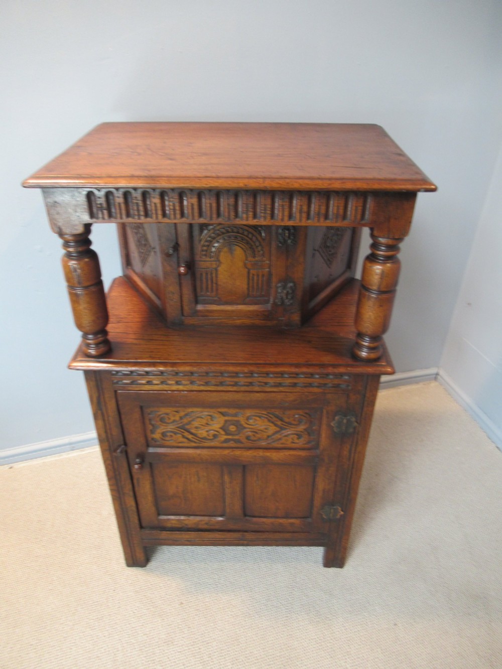 A small carved dark oak court cupboard featuring a two-tiered structure with turned bulbous supports and carved panel doors. View III