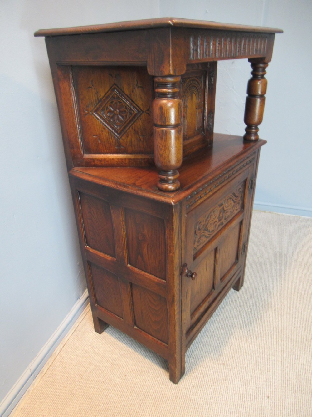 A small carved dark oak court cupboard featuring a two-tiered structure with turned bulbous supports and carved panel doors. View V