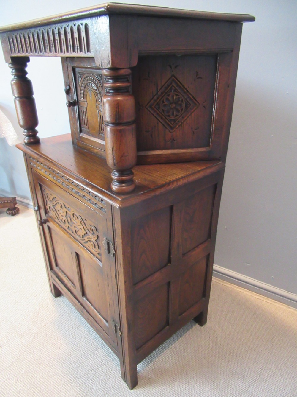 A small carved dark oak court cupboard featuring a two-tiered structure with turned bulbous supports and carved panel doors. View VI