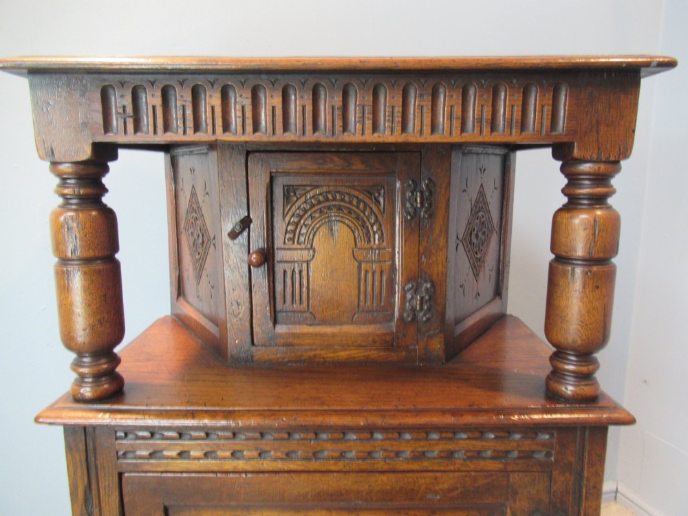 A small carved dark oak court cupboard featuring a two-tiered structure with turned bulbous supports and carved panel doors. View VII