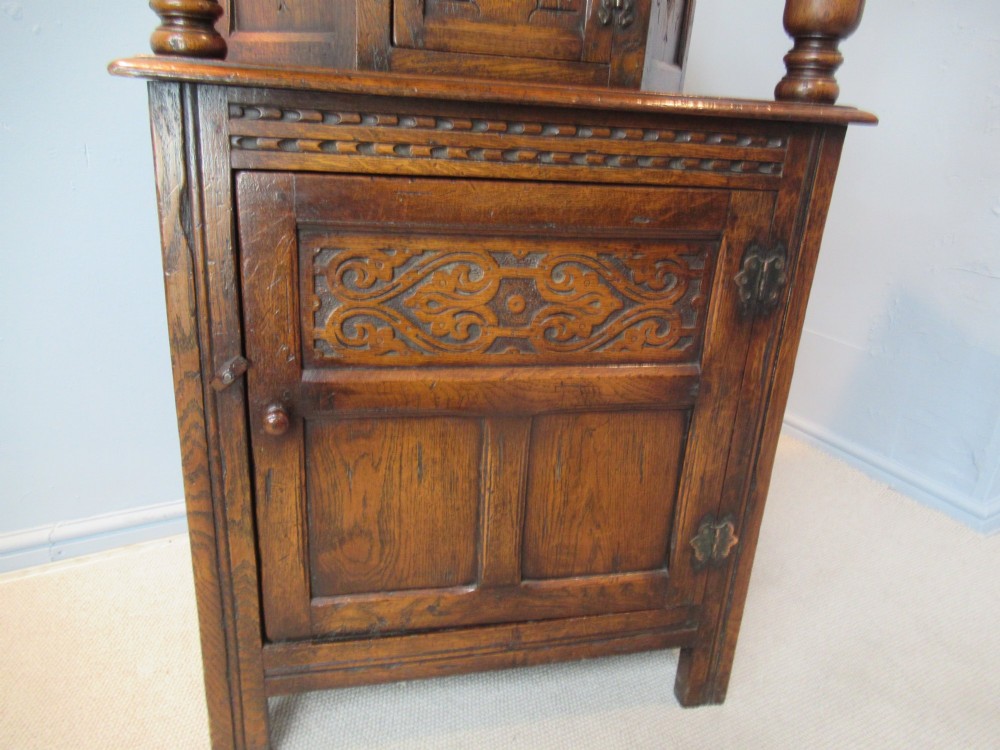 A small carved dark oak court cupboard featuring a two-tiered structure with turned bulbous supports and carved panel doors. View IX