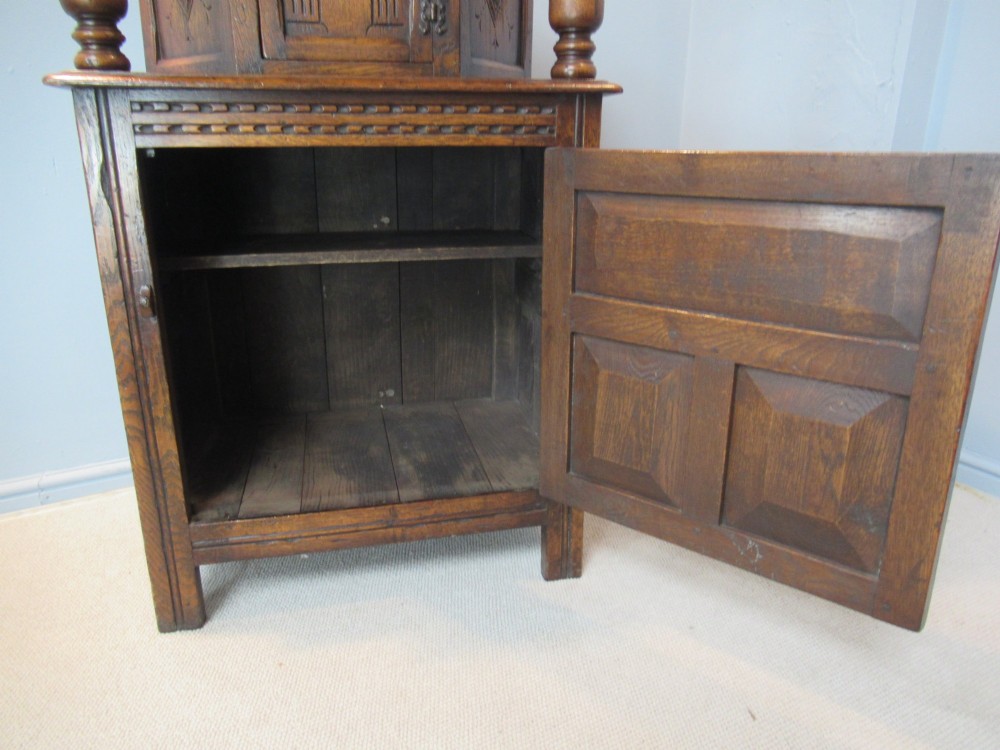 A small carved dark oak court cupboard featuring a two-tiered structure with turned bulbous supports and carved panel doors. View X