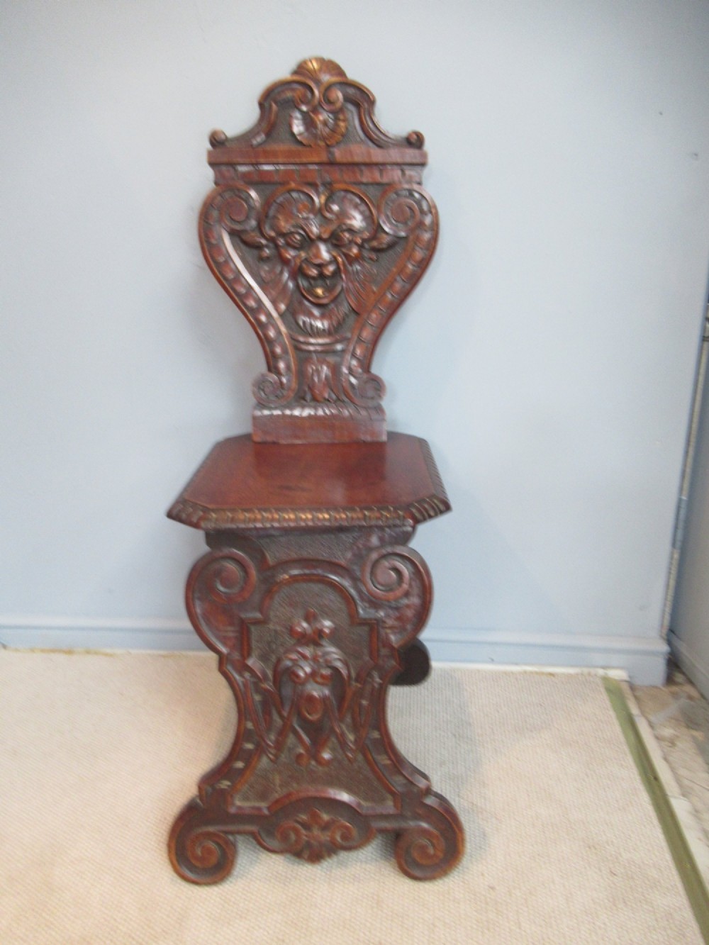 A Victorian carved mahogany hall chair featuring a detailed lion head mask sculpted into the backrest and a solid timber seat. View II