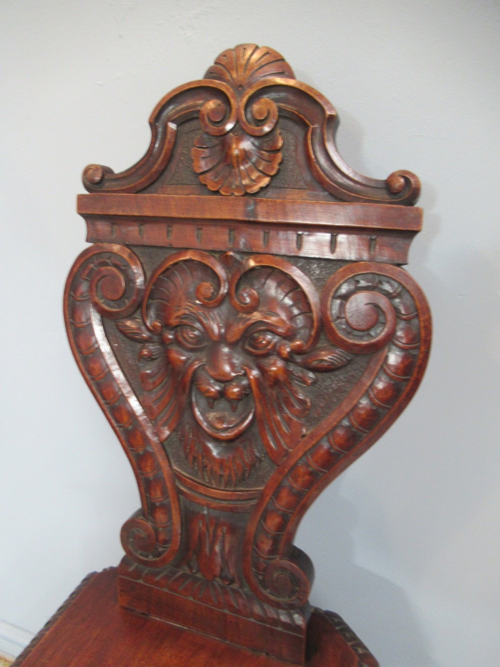 A Victorian carved mahogany hall chair featuring a detailed lion head mask sculpted into the backrest and a solid timber seat. View X