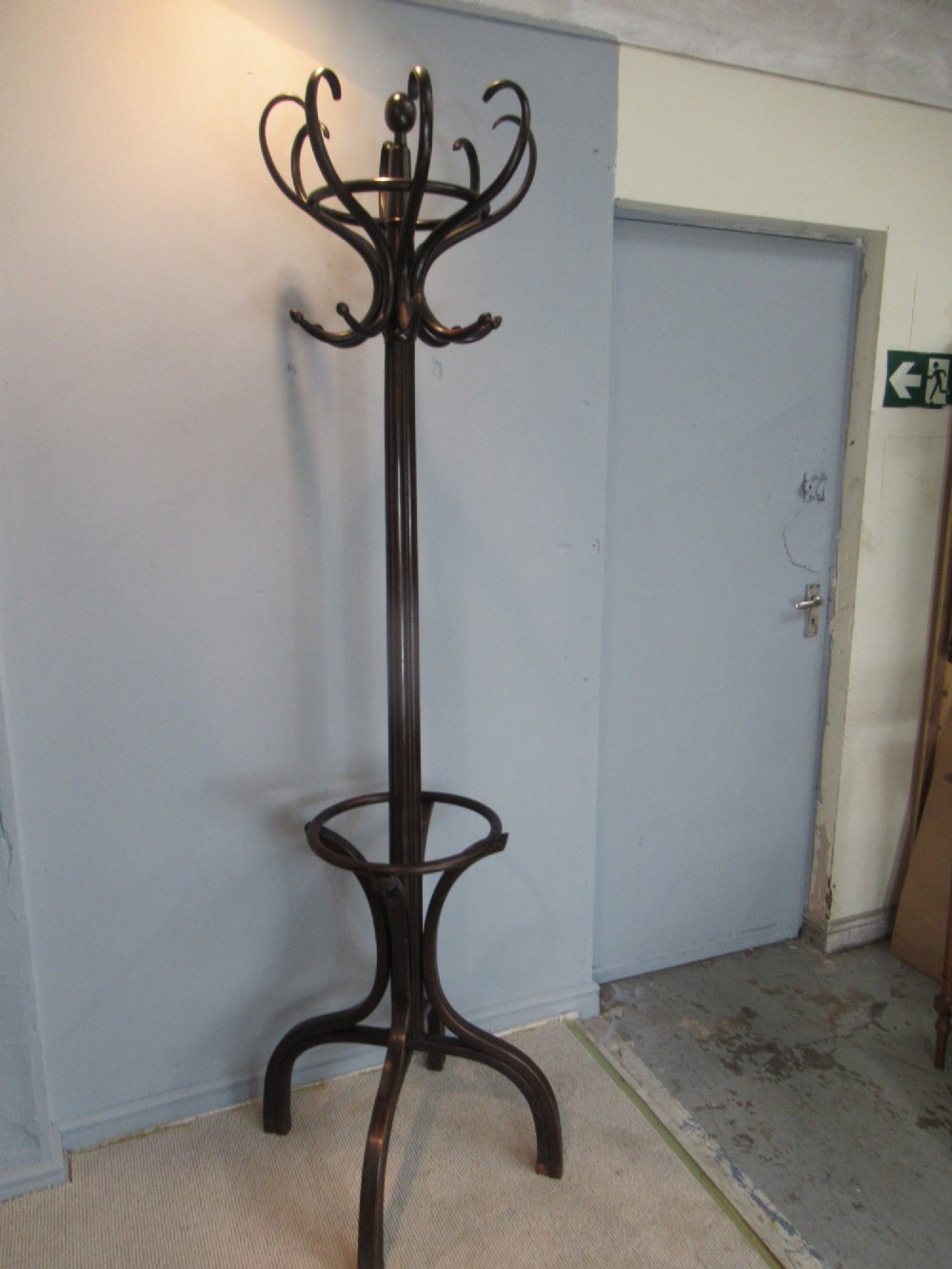 A dark brown bentwood hat and coat stand with upper curved hooks, a turned central stem, a lower umbrella ring, and four splayed feet.