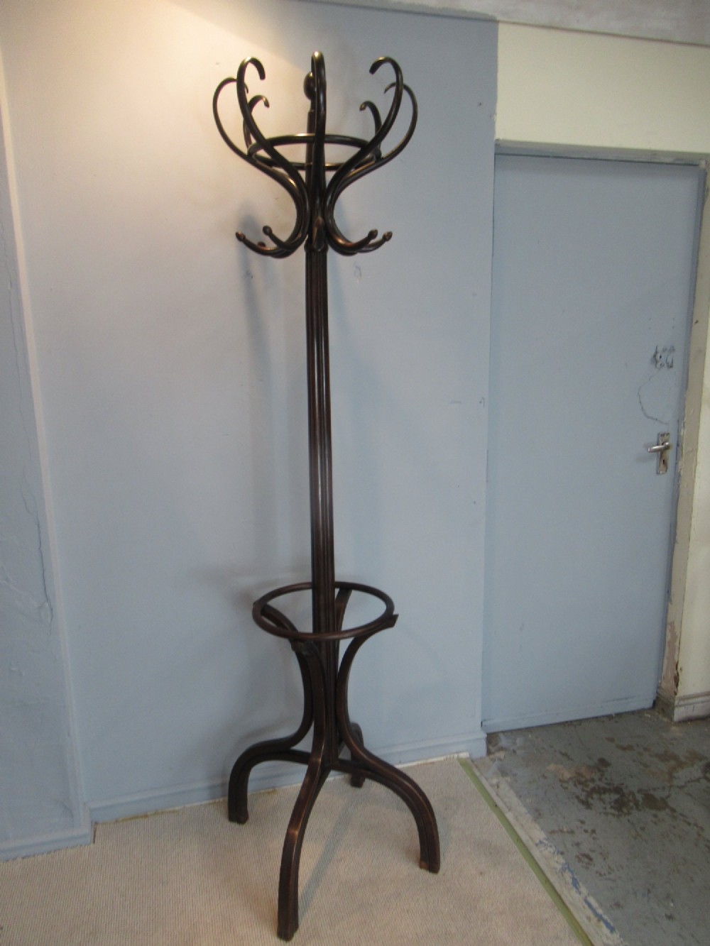 A dark brown bentwood hat and coat stand with upper curved hooks, a turned central stem, a lower umbrella ring, and four splayed feet. View II