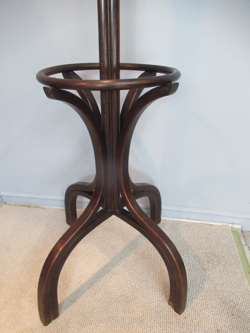 A dark brown bentwood hat and coat stand with upper curved hooks, a turned central stem, a lower umbrella ring, and four splayed feet. View III