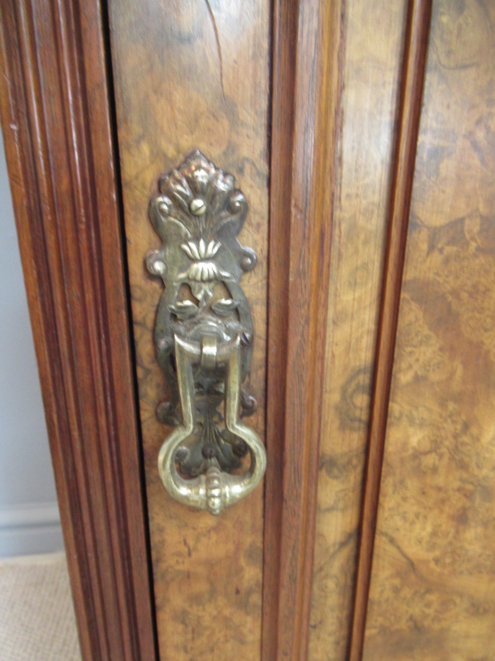 A late Victorian burr walnut bedside cabinet featuring a single panelled door with a brass drop handle, a shaped pediment gallery, and a plinth base on bun feet. View IV