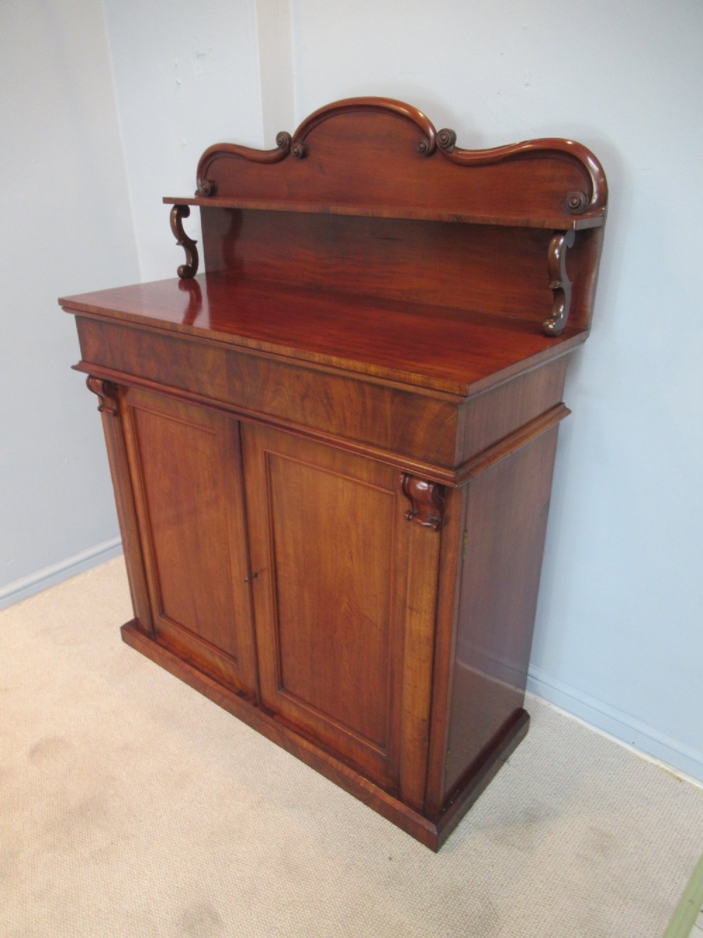 A Victorian mahogany chiffonier with a raised gallery shelf supported by carved scrolls above a two-door cabinet on a solid plinth base.
