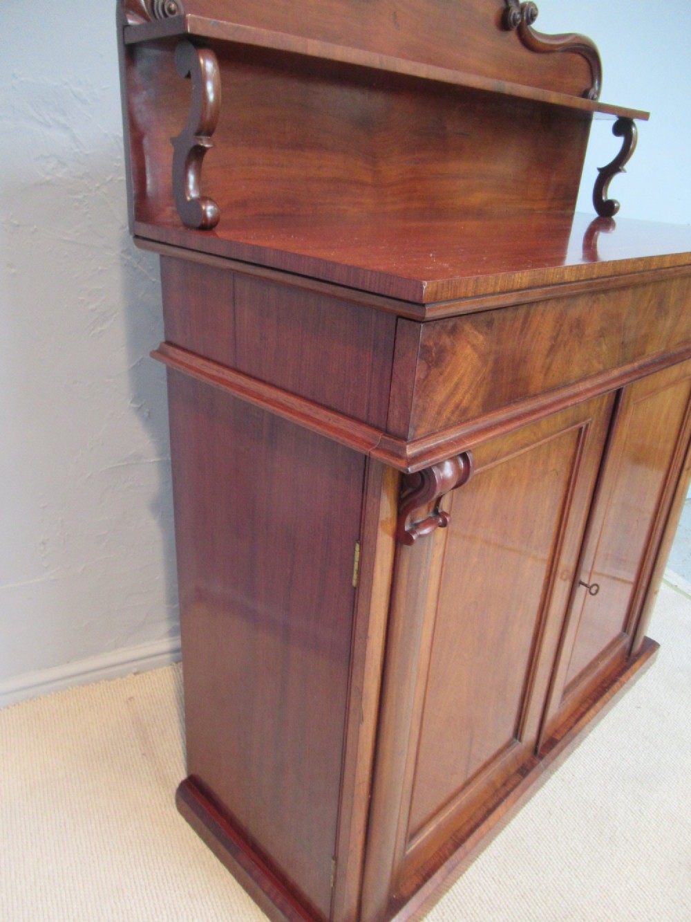 A Victorian mahogany chiffonier with a raised gallery shelf supported by carved scrolls above a two-door cabinet on a solid plinth base. View III