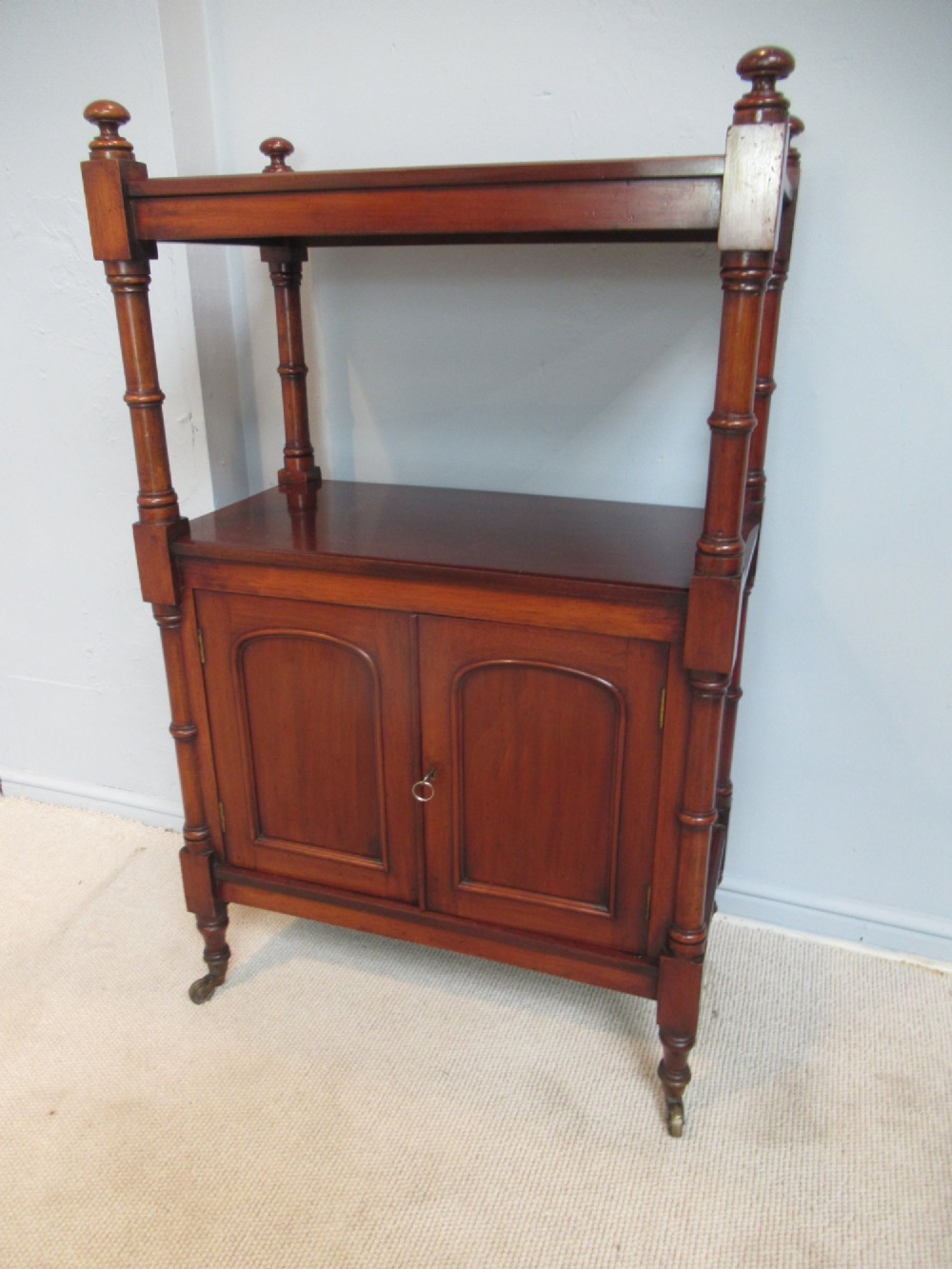 A Victorian mahogany chiffonier cabinet featuring a raised top tier supported by turned pillars above a two-door lower cupboard on brass castors.
