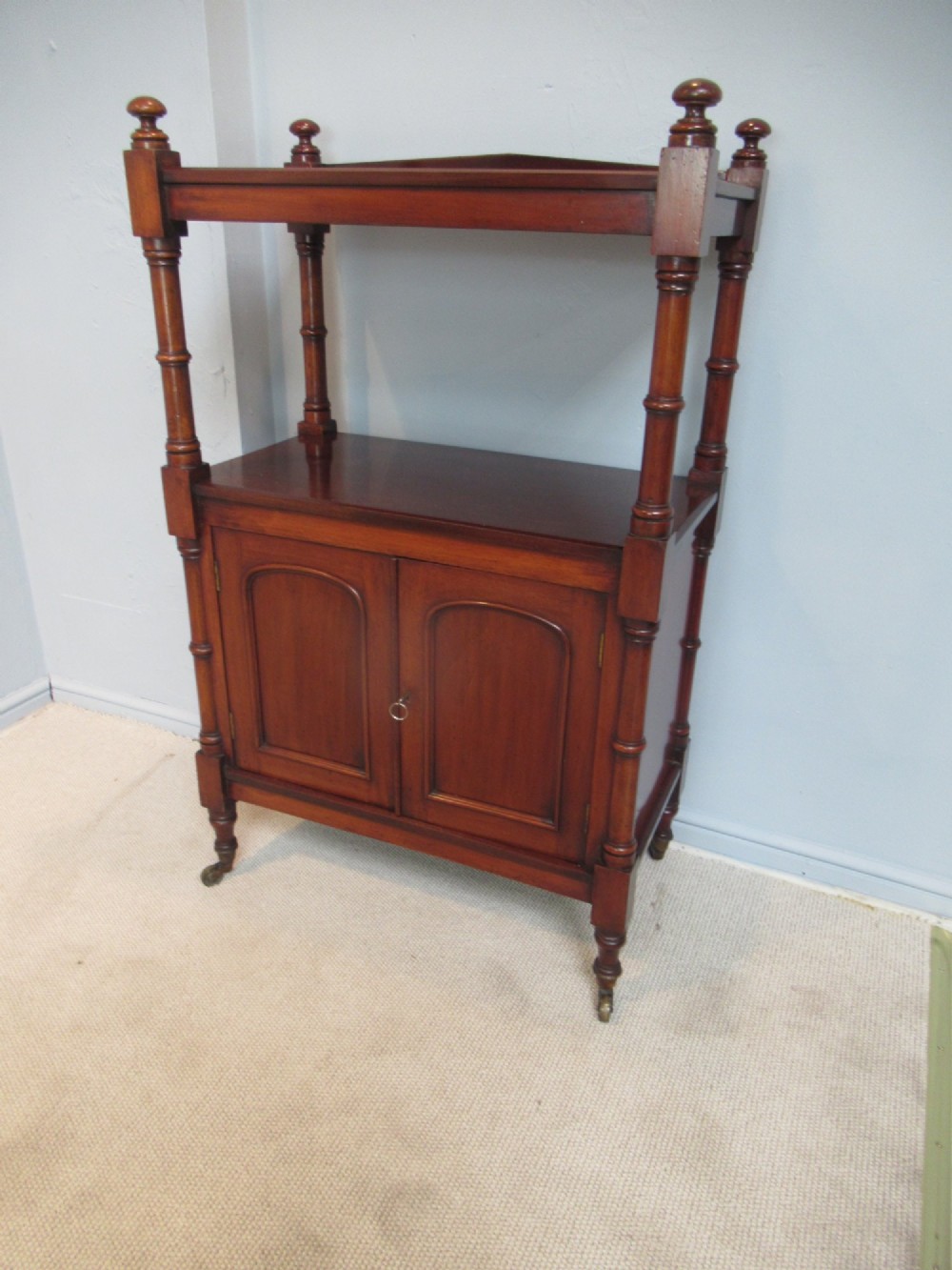 A Victorian mahogany chiffonier cabinet featuring a raised top tier supported by turned pillars above a two-door lower cupboard on brass castors. View II